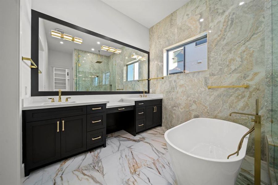 This elegant master bathroom is a perfect blend of luxury and sophistication. Featuring a dual-sink vanity with sleek black cabinetry and gold hardware, it offers ample storage and style. The freestanding soaking tub, paired with a modern gold faucet, adds a spa-like touch, while the oversized frameless glass shower and stunning marble-inspired tile walls complete the luxurious aesthetic. This master bath is a true retreat for relaxation and comfort.