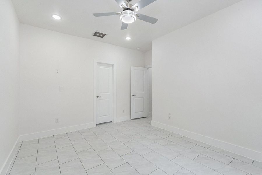 This room features a clean, modern design with neutral walls and tiled flooring. It includes recessed lighting, a ceiling fan, and two white doors, offering a bright and airy space suitable for various uses. This room features a clean, modern design with neutral walls and tiled flooring. It includes recessed lighting, a ceiling fan, and two white doors, offering a bright and airy space suitable for various uses.