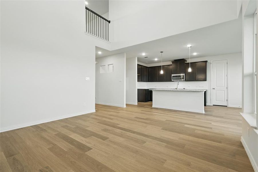 Unfurnished living room with light wood-style floors, baseboards, recessed lighting, and a high ceiling Unfurnished living room with light wood-style floors, baseboards, recessed lighting, and a high ceiling