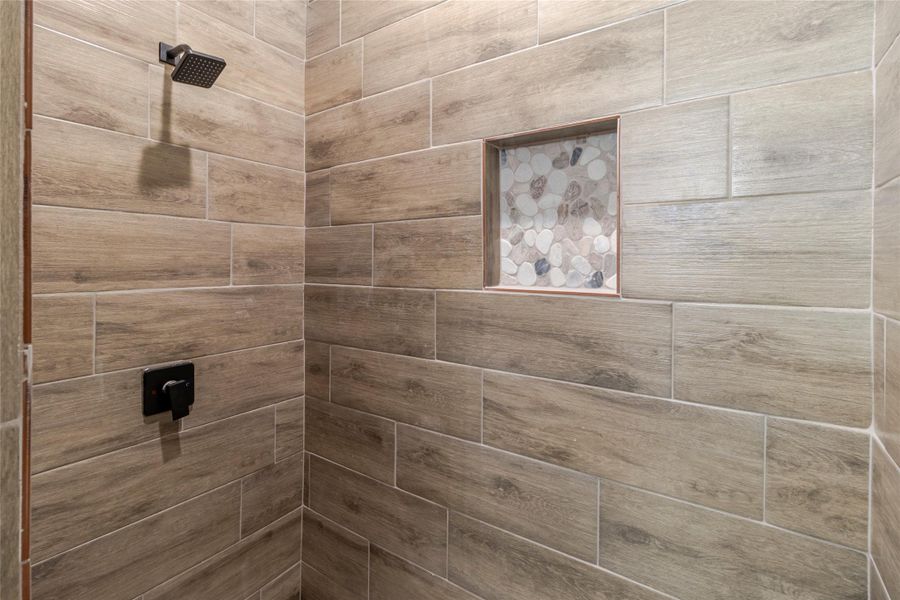 The primary shower is wrapped in floor too ceiling tile surround, with a recessed niche and matte-black fixtures. The primary shower is wrapped in floor too ceiling tile surround, with a recessed niche and matte-black fixtures.