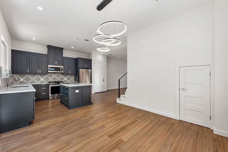 Kitchen featuring decorative light fixtures, decorative backsplash, appliances with stainless steel finishes, a center island, and light wood-style floors