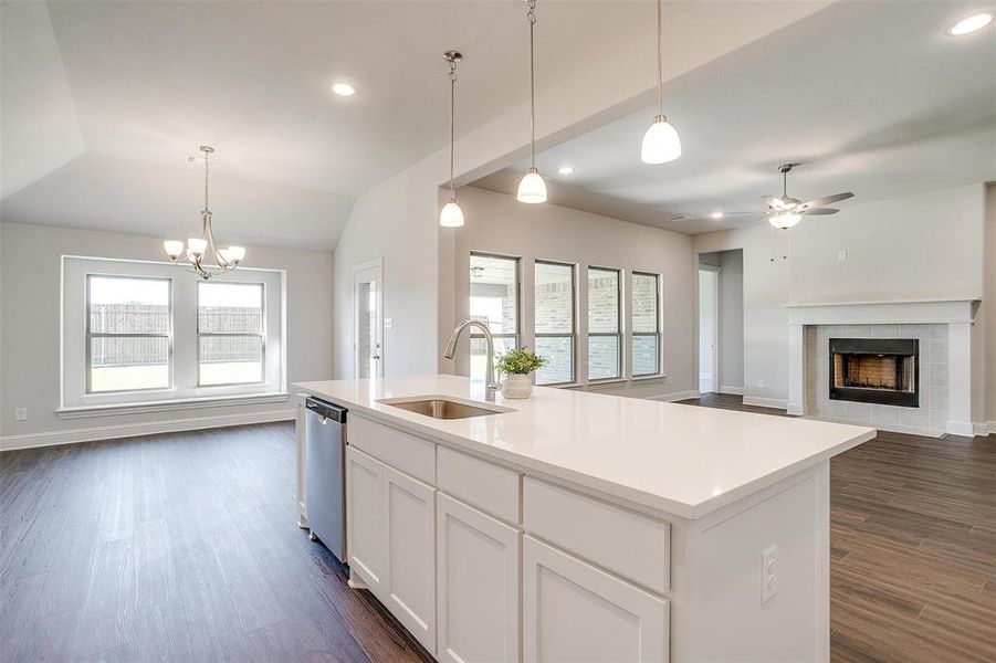 Kitchen with sink, a kitchen island with sink, dark wood-type flooring, a fireplace, and ceiling fan with notable chandelier