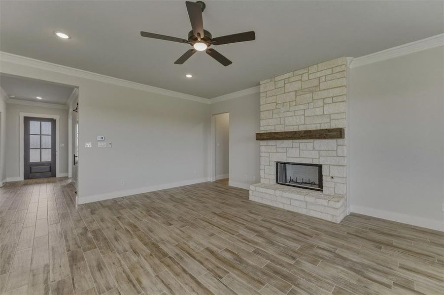 Living space featuring a stone-clad fireplace with wood mantel, wood-finish flooring, recessed lighting, crown molding, and a ceiling fan Living space featuring a stone-clad fireplace with wood mantel, wood-finish flooring, recessed lighting, crown molding, and a ceiling fan