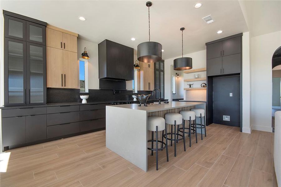 Kitchen with a breakfast bar, open shelves, decorative light fixtures, light brown cabinetry, and wood tiled floors Kitchen with a breakfast bar, open shelves, decorative light fixtures, light brown cabinetry, and wood tiled floors