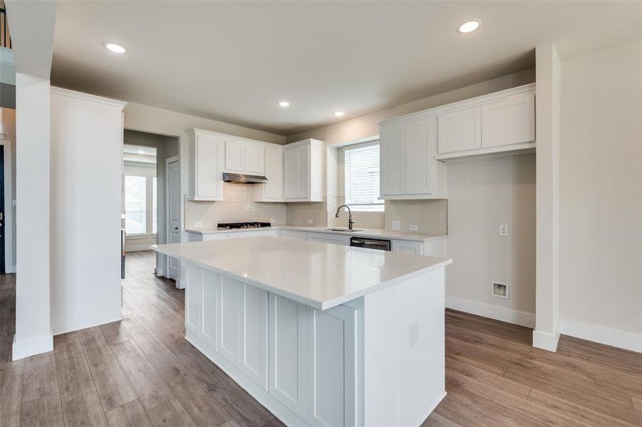 Kitchen featuring under cabinet range hood, a sink, gas cooktop, light countertops, and recessed lighting Kitchen featuring under cabinet range hood, a sink, gas cooktop, light countertops, and recessed lighting