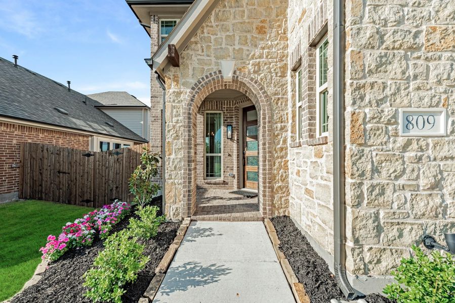 Stone and brick home exterior with arched entryway, walkway, and flower beds at house number 809