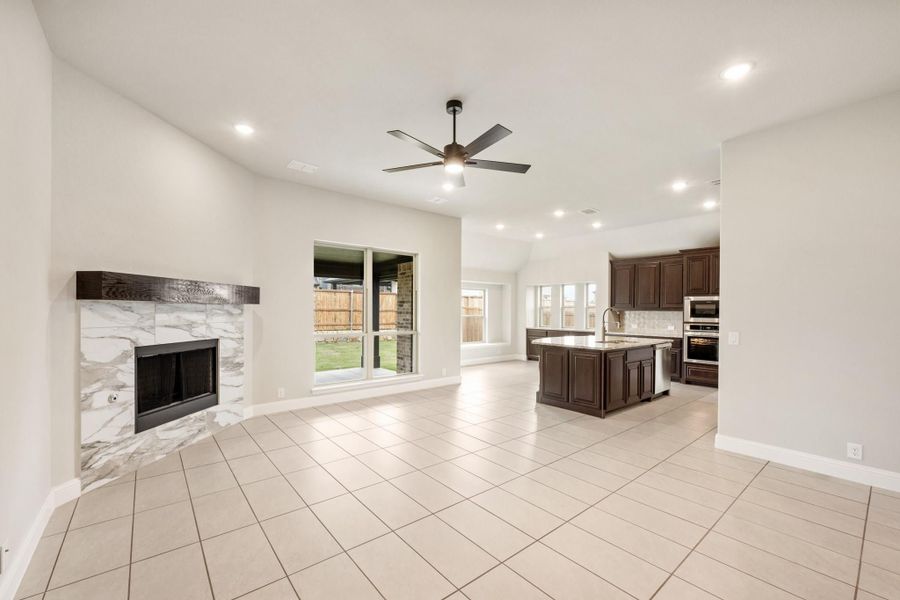 Open living area with marble fireplace, tile floors, and kitchen with dark cabinets and island Open living area with marble fireplace, tile floors, and kitchen with dark cabinets and island