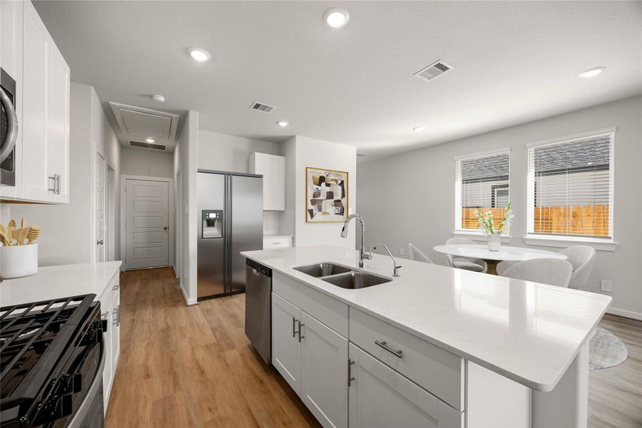 This bright, modern kitchen features white cabinetry, quartz countertops, and stainless steel appliances. The large island offers additional prep space and overlooks the dining area filled with natural light, perfect for casual meals or entertaining.
