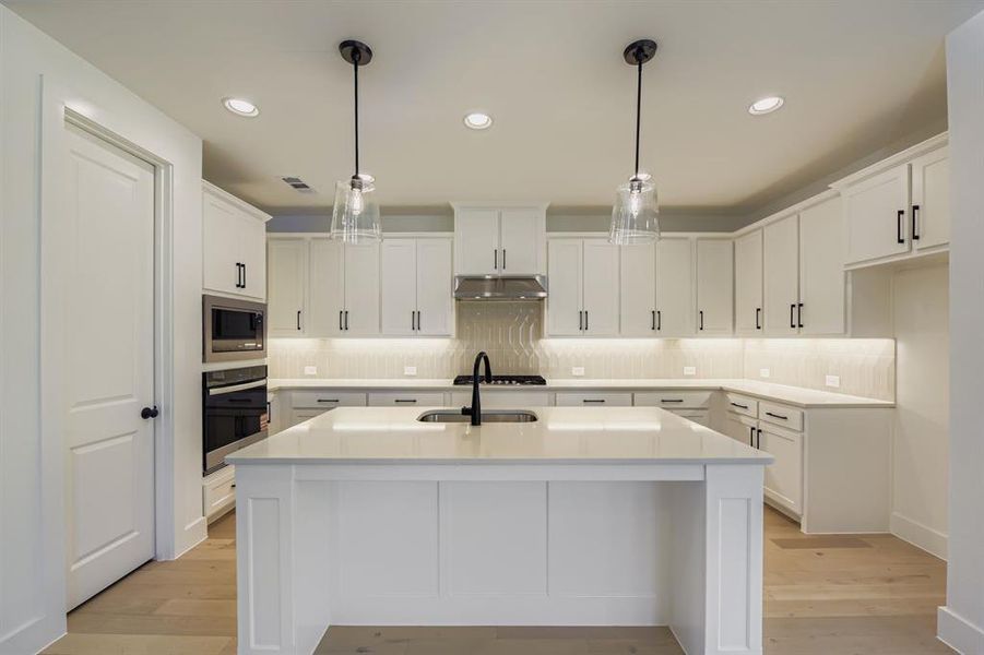 Kitchen with an island with sink, white cabinets, and hanging light fixtures