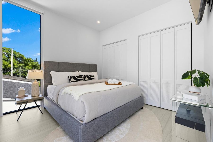 Floor-to-ceiling window, wood-finish flooring, and dual bi-fold closet doors with louvered detailing