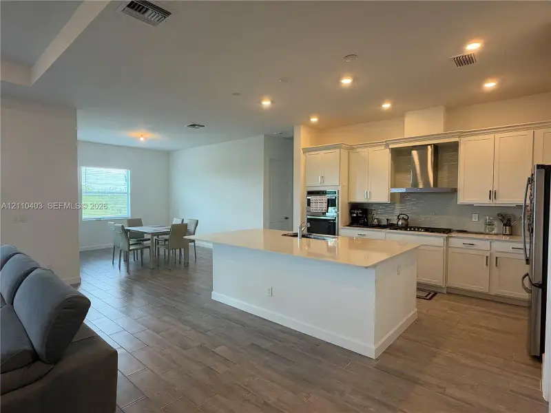 Kitchen featuring white shaker-style cabinetry, quartz countertops, a central island, stainless steel appliances, and wood-finish flooring