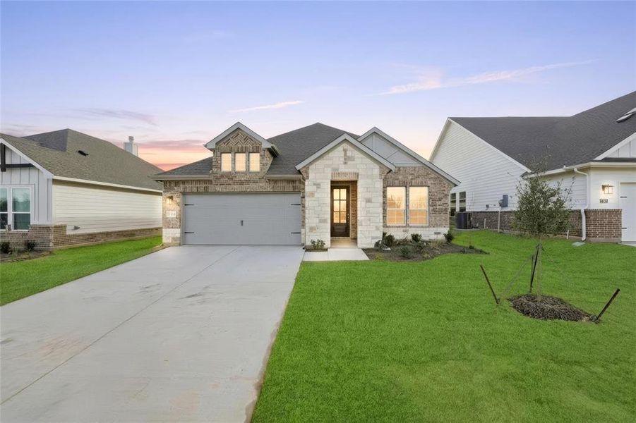 View of front of home with stone siding, concrete driveway, a yard, and a garage