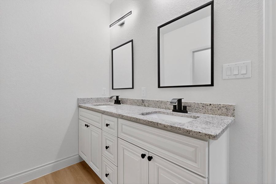 Double vanity featuring white shaker-style cabinetry, a light-toned speckled countertop, integrated sinks, and matte black fixtures Double vanity featuring white shaker-style cabinetry, a light-toned speckled countertop, integrated sinks, and matte black fixtures