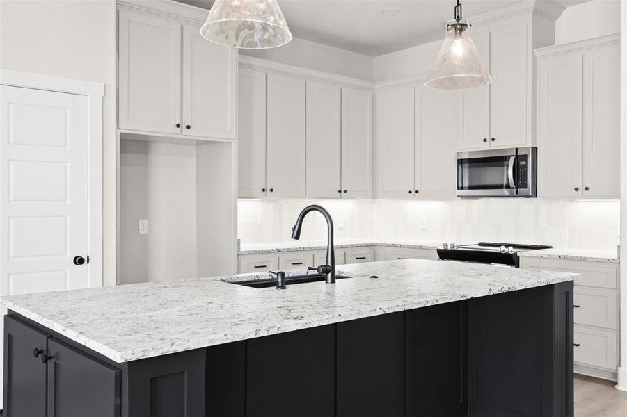 Kitchen featuring dark cabinetry, decorative light fixtures, stainless steel microwave, white cabinets, and an island with sink Kitchen featuring dark cabinetry, decorative light fixtures, stainless steel microwave, white cabinets, and an island with sink