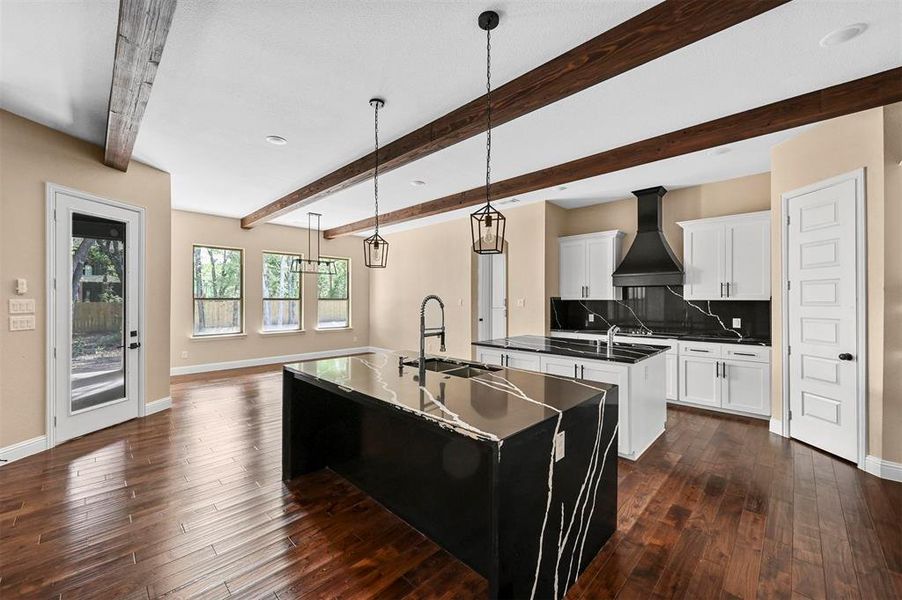 Kitchen featuring beam ceiling, custom range hood, dark hardwood / wood-style flooring, an island with sink, and sink