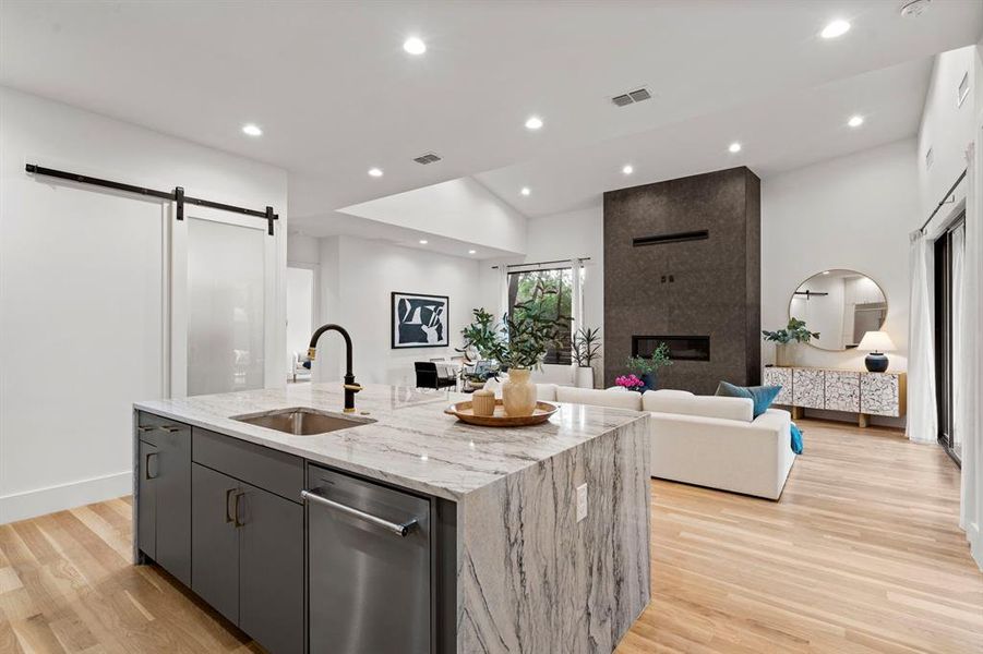 Kitchen with a barn door, stainless steel dishwasher, open floor plan, light wood-type flooring, and an island with sink Kitchen with a barn door, stainless steel dishwasher, open floor plan, light wood-type flooring, and an island with sink