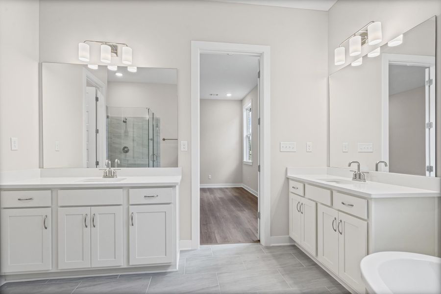 Bathroom featuring a shower stall, two vanities, and light wood finished floors
