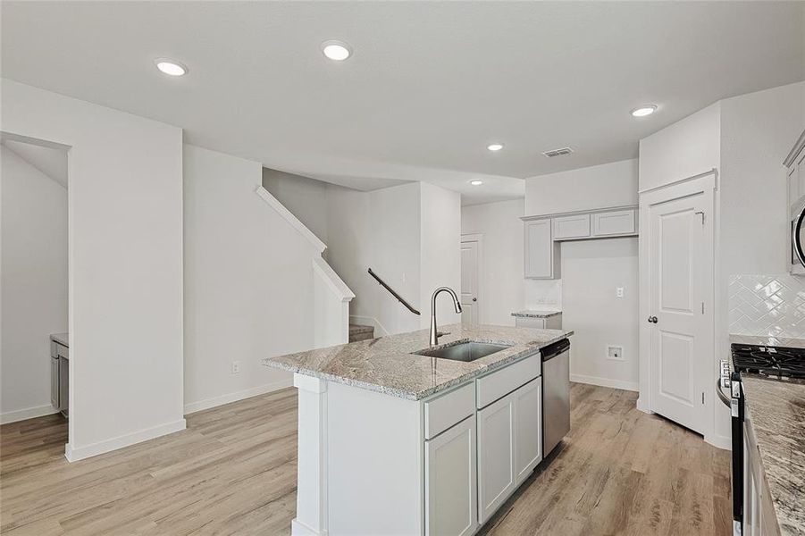 Kitchen with light stone countertops, sink, appliances with stainless steel finishes, light hardwood / wood-style flooring, and a kitchen island with sink