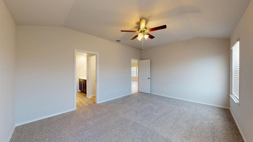 Spacious bedroom featuring vaulted ceilings, light-colored carpeting, and a ceiling fan with integrated lighting