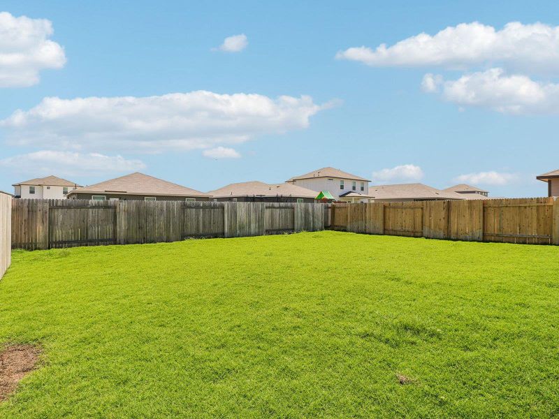 An expansive green lawn sits enclosed by a wooden privacy fence under blue skies.