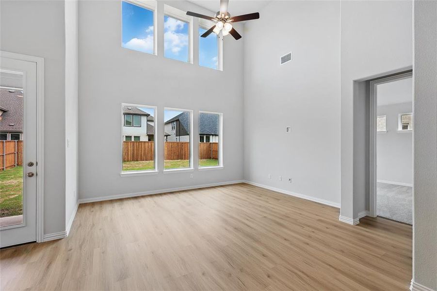 Unfurnished living room with light wood-style floors, visible vents, ceiling fan, and a high ceiling Unfurnished living room with light wood-style floors, visible vents, ceiling fan, and a high ceiling