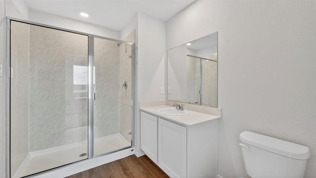 Contemporary bathroom featuring a glass-enclosed shower with light-toned tiled walls, a white single-sink vanity with a light countertop, a wall-mounted mirror, recessed lighting, and wood-finish flooring