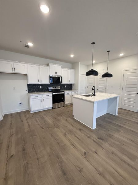 Kitchen featuring white cabinetry, stainless steel appliances, hanging light fixtures, a kitchen island with sink, and dark wood-type flooring