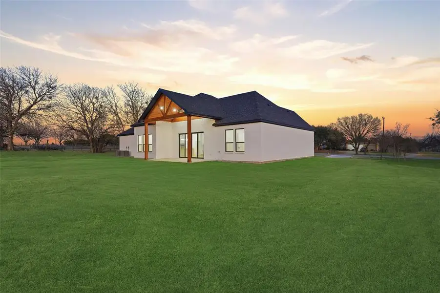 Back of house at dusk featuring a patio, a lawn, and stucco siding
