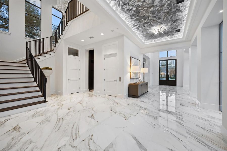 View looking towards the front door and foyer showcasing the stunning ceiling design and lighting. Grand staircase leads to the 2nd floor.