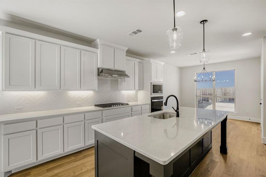 Kitchen with a center island with sink, light wood-style floors, a chandelier, two tone color scheme, and backsplash