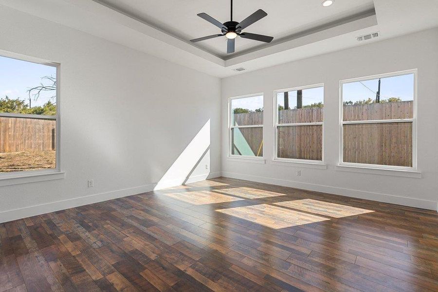 Unfurnished room featuring dark wood-style floors, ceiling fan, and a tray ceiling