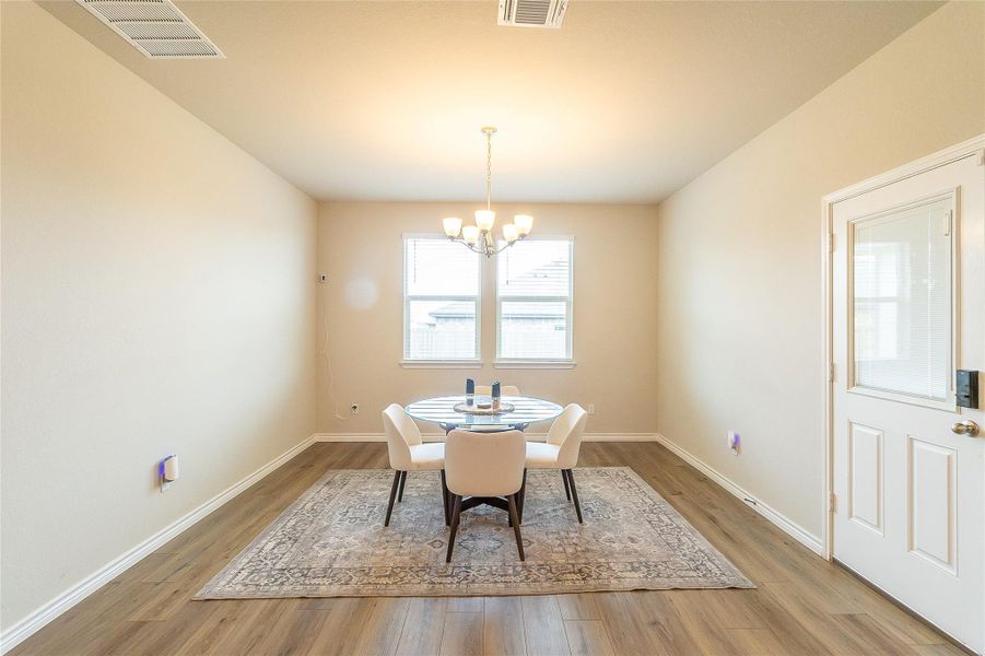 A refined dining space awaits, featuring wide plank flooring and a classic chandelier illuminating the setting.