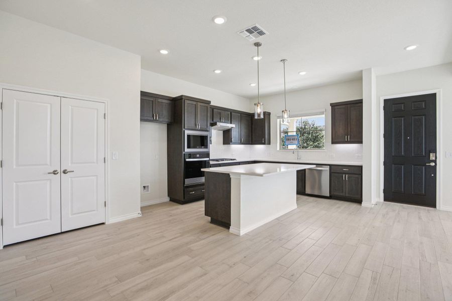 Kitchen featuring a kitchen island, stainless steel appliances, hanging light fixtures, dark brown cabinets, and recessed lighting