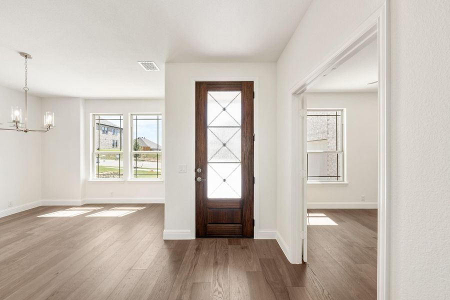 Entryway with dark wood front door, glass panels, hardwood floors, and chandelier in adjacent dining area Entryway with dark wood front door, glass panels, hardwood floors, and chandelier in adjacent dining area