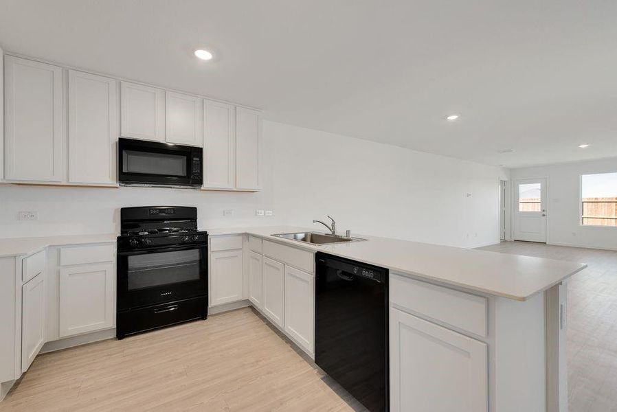 Kitchen featuring a peninsula, black appliances, recessed lighting, light countertops, and white cabinets