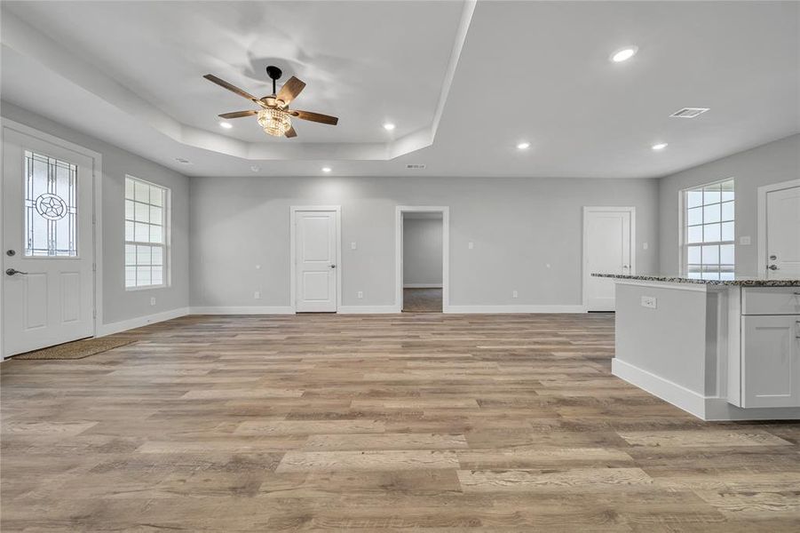 Unfurnished living room with light hardwood / wood-style floors, a raised ceiling, and ceiling fan