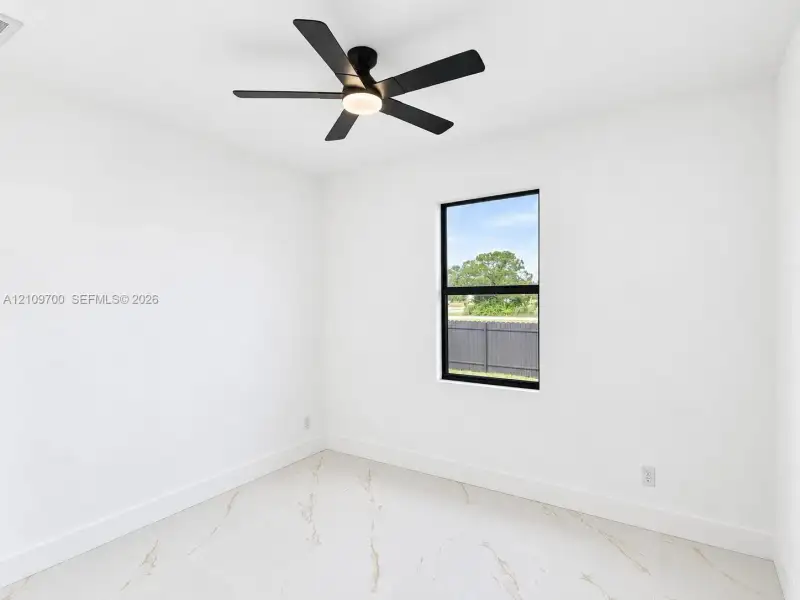 Interior space featuring large-format tile flooring with marble-style veining, a matte black ceiling fan with integrated lighting, and a window with a matte black frame