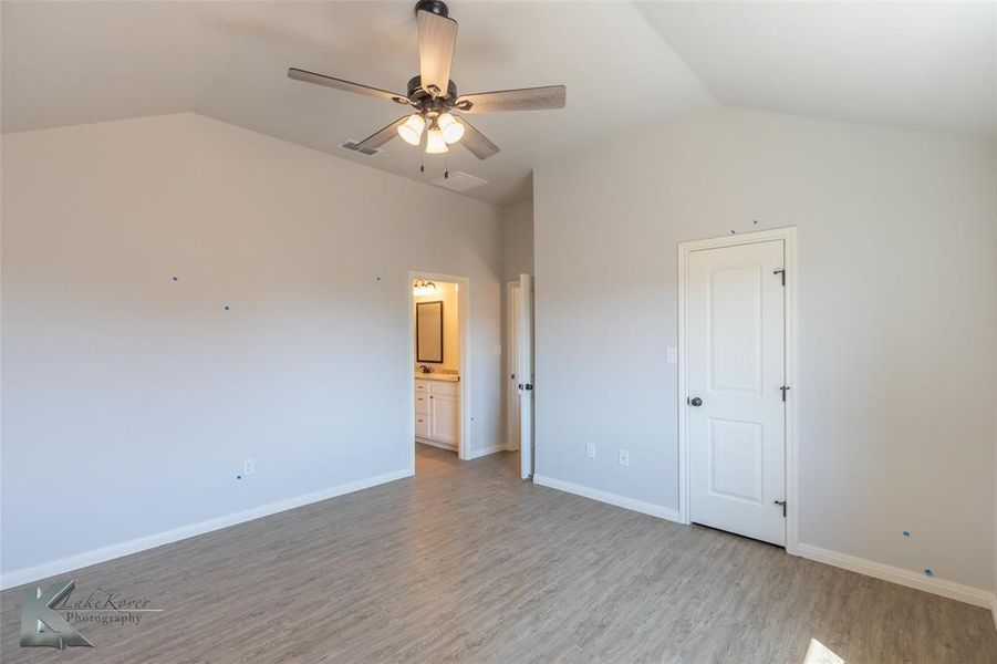 Unfurnished bedroom featuring vaulted ceiling, light wood-type flooring, a ceiling fan, and connected bathroom