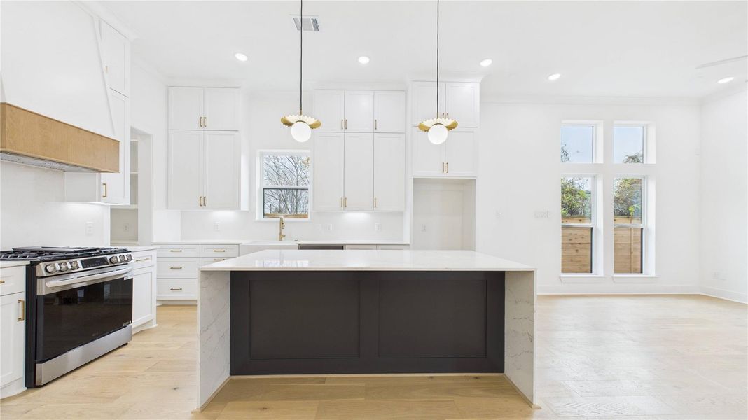 Grand quartz waterfall island with pop-up electrical receptor. Cabinets to the ceiling. Even the backsplash is quartz. Gold and white accents abound.
