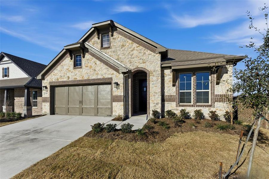French country style house with stone siding, concrete driveway, brick siding, and a garage