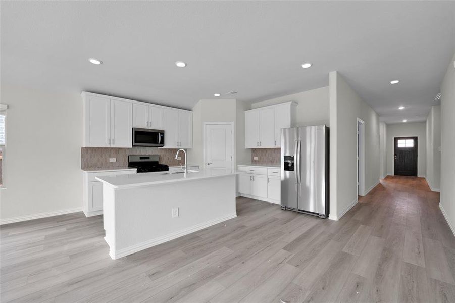 Kitchen with decorative backsplash, appliances with stainless steel finishes, white cabinets, a kitchen island with sink, and recessed lighting Kitchen with decorative backsplash, appliances with stainless steel finishes, white cabinets, a kitchen island with sink, and recessed lighting