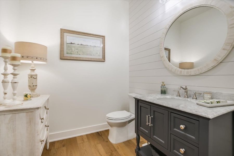 Half bathroom with vanity, wood finished floors, baseboards, toilet, and wooden walls Half bathroom with vanity, wood finished floors, baseboards, toilet, and wooden walls