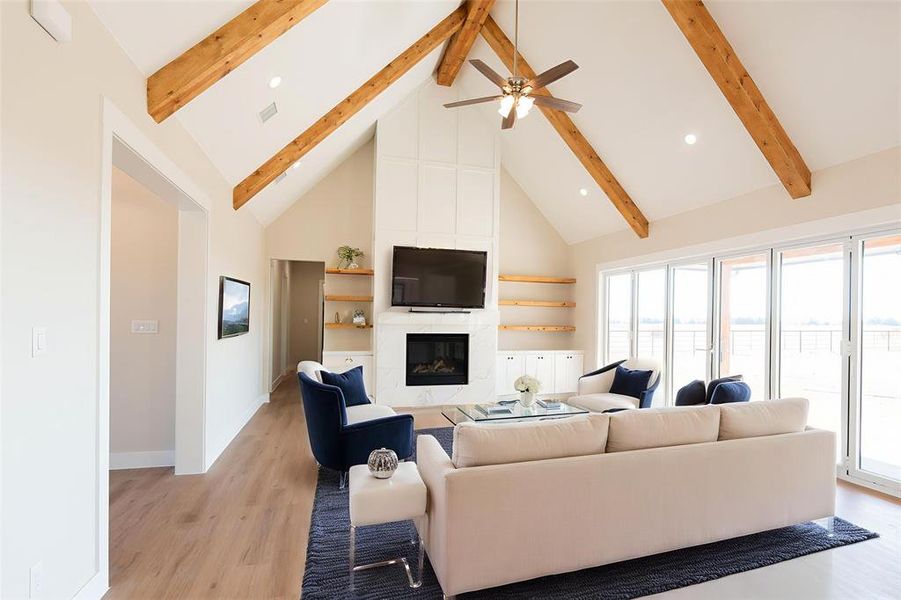 Living area with high vaulted ceiling, a large fireplace, light wood-style flooring, ceiling fan, and beamed ceiling