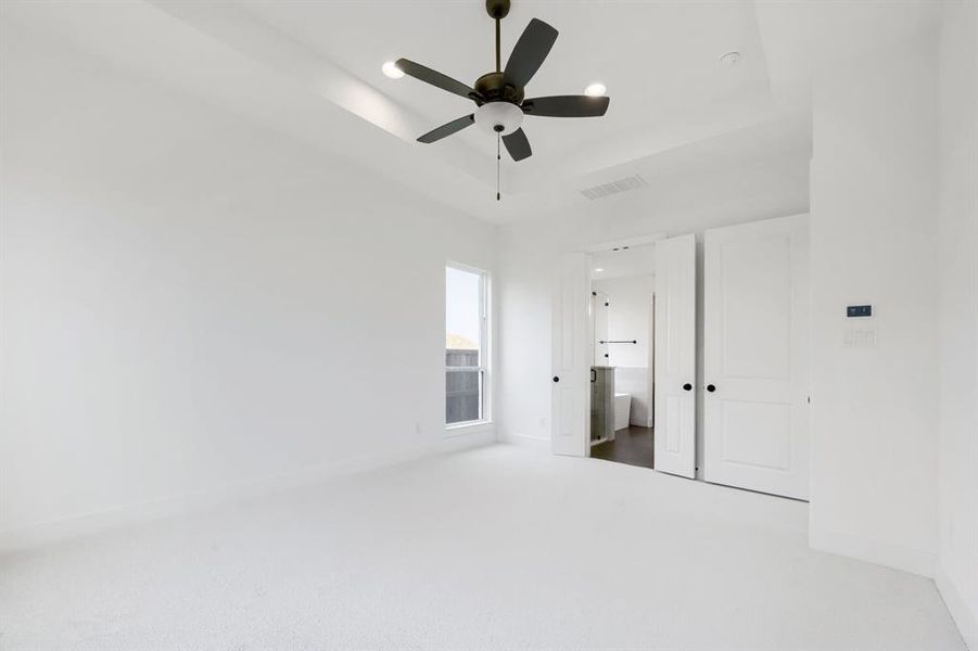 Spacious room featuring white carpeting, a tray ceiling with a ceiling fan, and a single window