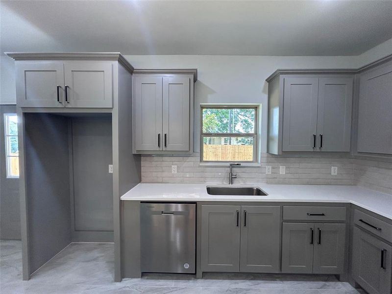 Kitchen with gray cabinets, stainless steel dishwasher, backsplash, and light countertops Kitchen with gray cabinets, stainless steel dishwasher, backsplash, and light countertops