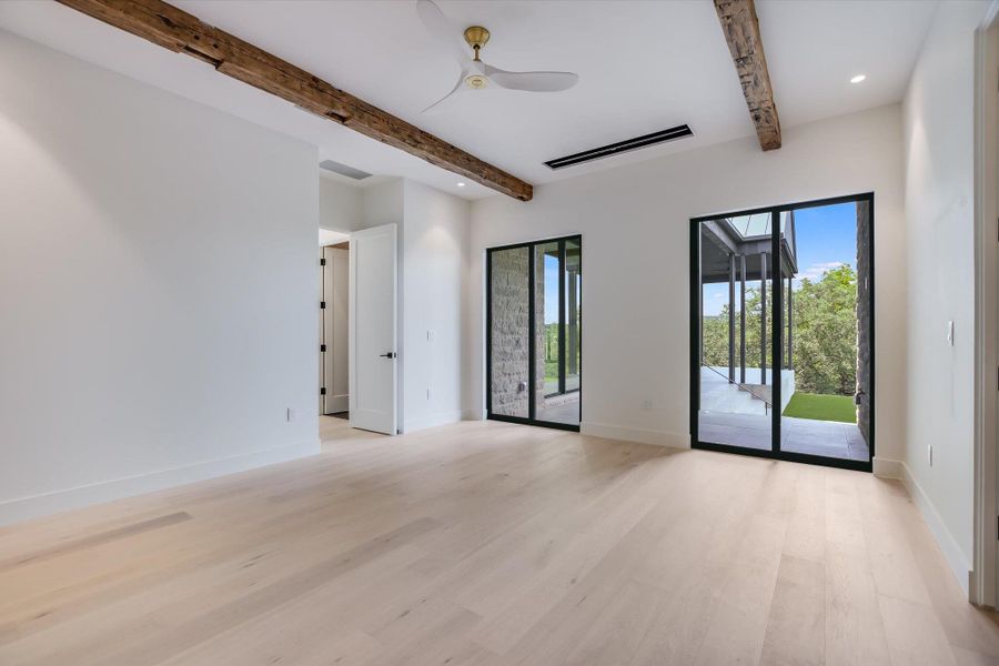 Exposed wood beams adorn the ceiling of this airy room with light wood floors and generous natural light from full-height glass doors.