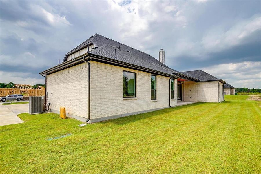 Back of property with central air condition unit and a lawn