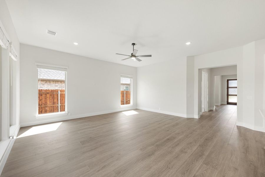 Open living room with light wood floors, ceiling fan, white walls, and two windows