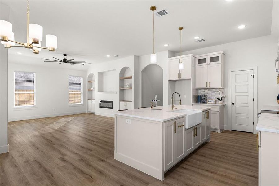 Kitchen with pendant lighting, sink, light stone counters, an island with sink, and white cabinets