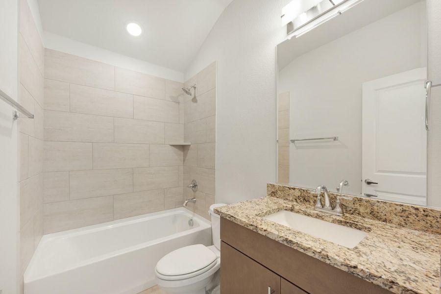 Bathroom with tiled tub-shower combo, granite vanity countertop, and dark wood cabinets